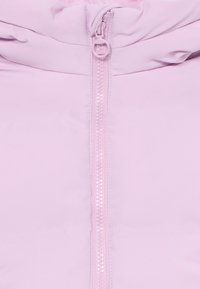 Chaqueta de cremallera de color rosa claro con una textura suave, cuello alto y cremallera a juego con tira de anillo. Las costuras cosidas aportan estructura.