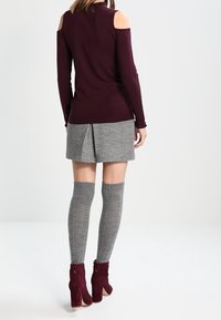 Burgunderfarbener Cold-Shoulder-Pullover, grauer, plissierter Rock, graue Kniestrumpf und burgunderfarbene Stiefeletten mit dicker Absatz. Strukturierte Stoffe verwendet.