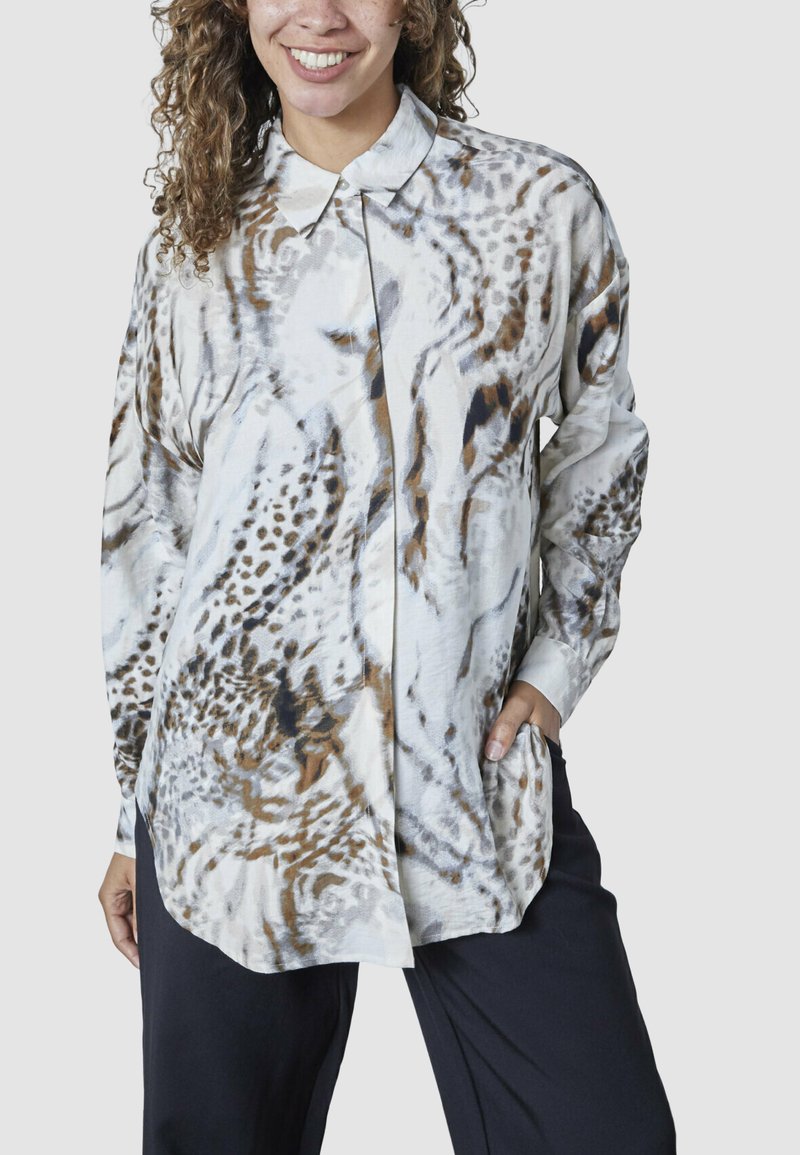 Langærmet bluse i let stof med en hvid bund og brune samt sorte dyreprintmønstre, frontknaplukning og sidelommer.