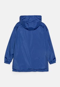 Giacca impermeabile blu con cappuccio, polsini elastici e vestibilità comoda. Tessuto liscio con dettagli minimi sul retro.