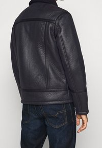 Svart läderjacka med en strukturerad yta, med hög krage och rundade sömmar, kombinerad med mörkblå jeans.