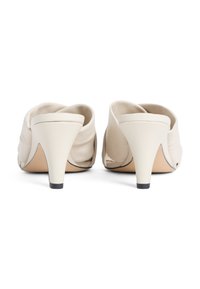 Μπεζ μπεζ δερμάτινα mules με στρογγυλεμένο σχήμ α, που διαθέτουν λεπτό τακούνι και απαλό, ρυτιδωτό υλικό στο πίσω μέρος. Διακοσμητικά στοιχεία με μαύρο περίγραμμα.