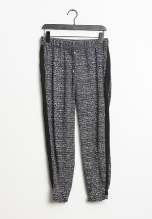 Schwarz-weiße, strukturierte Jogginghosen mit elastischem Bund und schwarzen Seitenstreifen, aufgehängt an einem schwarzen Bügel vor weißem Hintergrund.