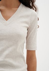 Beige gerippte V-Neck-Top mit kurzen Ärmeln, aus strukturiertem Stoff und mit figurbetontem Design. Keine sichtbaren Verschlüsse oder Muster.