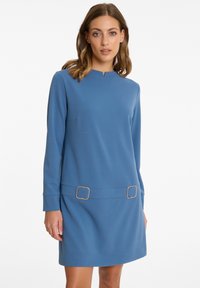 Blaues langärmeliges Kleid mit hohem Ausschnitt, zwei goldenen quadratischen Schnallen an der Taille und einem glatten, strukturierten Stoff.