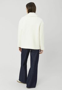 Veste blanche texturée avec un col classique, une coupe légèrement oversize et des détails de couture au dos, associée à un jean denim foncé à jambes larges.