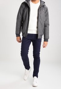 Grå huvtröja, vit texturerad tröja, marinblå slim-fit byxor och vita sneakers. Har dragkedjor och en avslappnad passform.