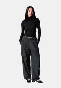 Haut ajusté à manches longues noir avec un col montant et un petit logo, associé à un pantalon noir ample et à des chaussures plates noires. Texture du tissu lisse.