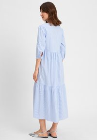 Hellblaue, gestreifte Midi-Kleid mit Dreiviertelärmeln, gerafftem Taillenausschnitt und Rüschensaum. Glattes Material mit seitlichen Ausschnitten.