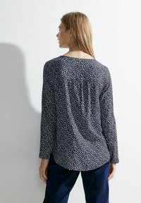 Blusa blu navy a maniche lunghe con un motivo geometrico bianco, dotata di scollatura rotonda e pieghe posteriori per una vestibilità rilassata.