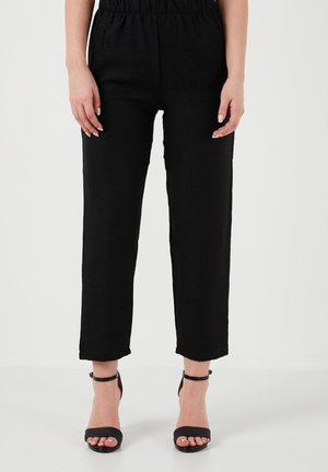 Black linen trousers with an elastic waistband, straight cut, and ankle length, paired with black strappy high-heeled sandals.
