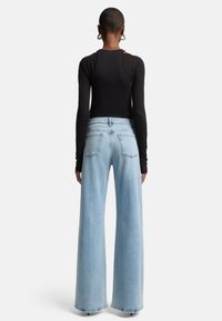 Zwarte lange mouwen top gecombineerd met lichtblauwe wijde jeans met een hoge taille en achterzakken, met een gladden denimtextuur.