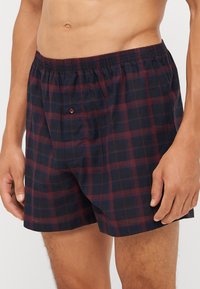 Boksershorts i bomull med et marineblått og burgunder rutemønster, med elastisk midjebånd og en enkelt knappelukking foran.