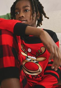 Red and black plaid pajama set featuring a cartoon reindeer with sunglasses, wearing a Santa hat, on the front. Soft fabric with ribbed cuffs.