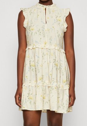 Ärmelloses cremefarbenes Kleid mit kleinem gelb-blauem Blumenmuster, gestuften Rüschen und einem Schlüsselloch-Ausschnitt bei einer dunkelhäutigen Person.