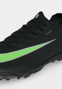 Μαύρο ποδοσφαιρικό παπούτσι Nike Flyknit με φωτεινό πράσινο swoosh και κορδόνια, με υφασμένο πέλμα και μικρό πράσινο λογότυπο στη γλώσσα.