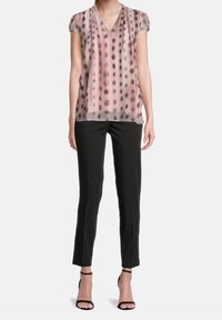 Chemisier rose transparent à pois noirs, décolleté en V, manches courtes, associé à un pantalon noir ajusté et des talons noirs à lanières.