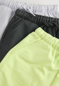 Tre par joggere i blødt stof: lys grå, mørk grå og neongrøn. Hver har en elastisk talje og sidelommer.