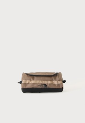 Prostokątna brązowo-czarna kosmetyczka The North Face z poziomym beżowym paskiem i zamkiem błyskawicznym u góry na jednolitym białym tle.