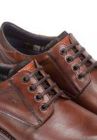 Zapatos de piel marrón con puntas redondas, seis ojales y cordones marrones oscuros. Presentan un collar texturizado y una sutil marca en la lengua.