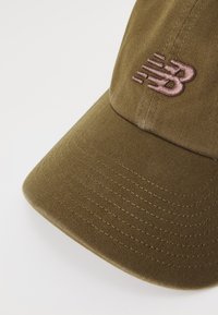 Olivengrønn baseballcap med buet skjerm og rosa brodert "NB"-logo på frontpanelet mot hvit bakgrunn.