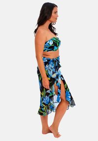 Top bandeau floral azul con fondo negro y falda envolvente de largo hasta los tobillos a juego. Presenta hojas verdes vibrantes y una textura fluida y transparente.