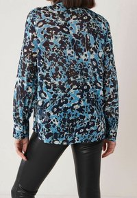 Sininen ja musta pitkähihainen pusero, jossa on abstrakti eläinkuos. Kevyt kangas, jossa on sileä pinta, napit hihansuissa ja väljä istuvuus.