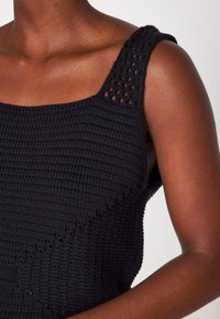 Ingrandimento di una persona che indossa un top senza maniche nero in maglia con un motivo testurizzato e traforato lungo la spallina.