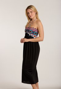 Schwarzes trägerloses Kleid mit bunt gesticktem Oberteil und Halterneck-Bindung. Fließender Stoff, in knielanger Länge, mit geometrischen Mustern und Akzenten.