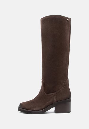 Bota castanha de camurça até ao joelho, com bico quadrado e salto bloco. Apresenta costura decorativa ao longo da costura superior e uma textura suave.