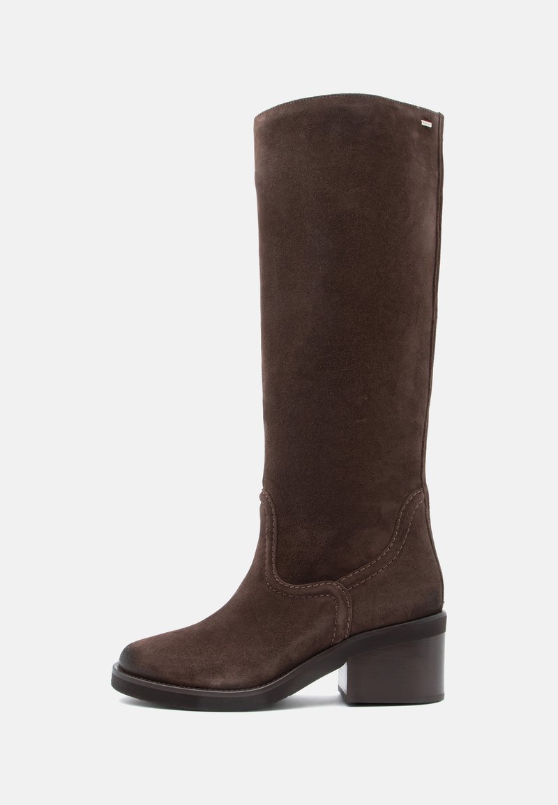 Bota alta de ante marrón con punta cuadrada y tacón de bloque. Presenta un bordado decorativo a lo largo de la costura superior y una textura suave.