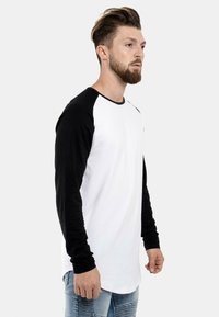 Langärmliges Raglan-T-Shirt mit schwarzen Ärmeln und weißem Körper, aus Baumwolle, mit Rundhalsausschnitt und lässiger Passform.