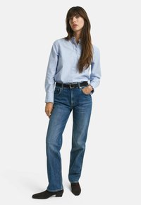 Ljusblå knäppt skjorta i kombination med mörkblå rakbenjeans. Svart bälte, strukturerat tyg och mörka skor fulländar outfiten.