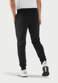 Schwarze Jogginghose mit schmalem Schnitt, elastischem Bund, Seitentaschen und Rippbündchen. Getragen mit weißen Sportschuhen.