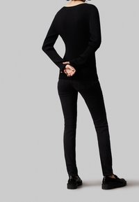 Svart ribbad långärmad tröja, åtsittande silhuett, matchad med smala svarta jeans och glänsande svarta skor, sedd bakifrån.