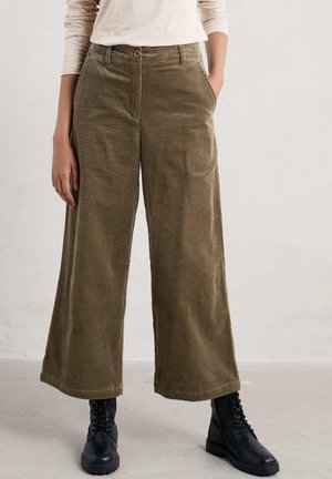 Pantalones anchos de pana verde oliva con tela texturizada, bolsillos delanteros y cierre de botón. Combinados con botas negras con cordones.