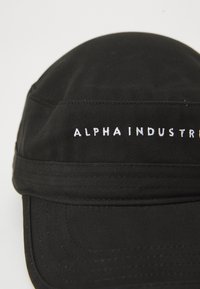Casquette en tissu noir avec visière incurvée, arborant le texte noirci 'ALPHA INDUSTR' brodé sur le panneau avant.