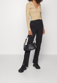 Beige ribbad långärmad topp med krage, ihop med svarta högmidjade jeans med sidofickor. Svart handväska i krokodilmönster och svarta sneakers.