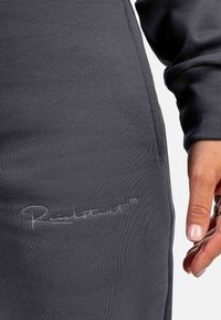 Graue gerippte Jogginghosen mit einem gestickten Logo-Detail an der Hüfte, weichem Material und figurbetontem Design, sowie sichtbaren Seitentaschen.