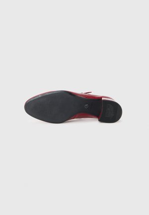 Semelle d'une chaussure habillée en cuir rouge avec semelle extérieure en caoutchouc noir texturé et petit talon, nom de la marque embossé sur la partie du talon.