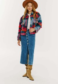 Pestrý károvaný kabátik s modrými, červenými a ružovými odtieňmi, kombinovaný s dlhou denimovou sukňou s zapínaním na gombíky a rozparkom, doplnený béžovými čižmami.