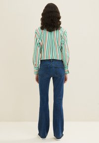 Gestreiftes, grünes, rotes und weißes Langarmshirt kombiniert mit blauen Schlagjeans, die eine glatte Textur und eine lässige Passform aufweisen.