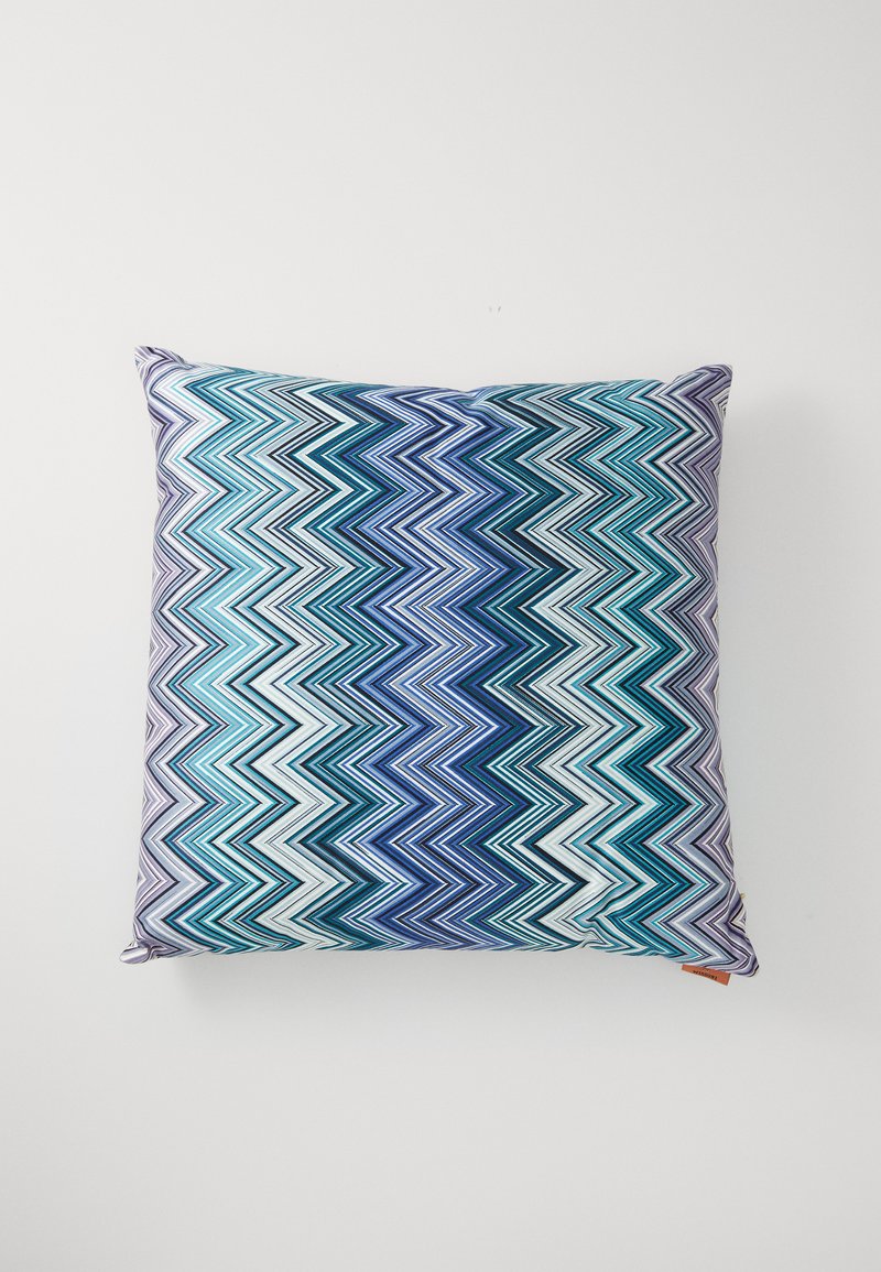 Τετράγωνο μαξιλάρι με σχέδιο ζιγκ-ζαγκ σε αποχρώσεις του μπλε, της τυρκουάζ και του λευκού. Κατασκευασμένο από υφασμάτινη επιφάνεια με υφή, διαθέτει ορατές ραφές και άκρες.