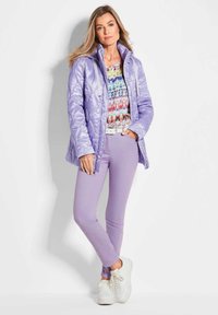 Licht paarse gewatteerde jas met een glanzende afwerking, multi-kleurige gemusterde top, paarse broek en witte sneakers. Casual pasvorm en ontwerp.
