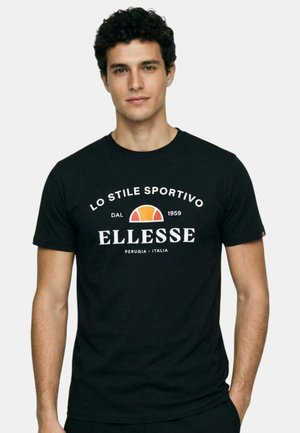 Jeune homme portant un t-shirt noir Elleesse avec texte blanc et logo en demi-cercle orange-rouge, debout devant un fond clair uni.