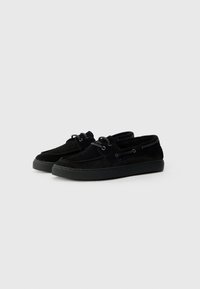 Sorte mokkasiner i nubuck med lav profil, avrundet tå, snøresystem og strukturert såle. Har minimal søm og mykt stoff.