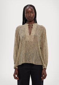 Lehounká halenka s dlouhými rukávy v béžové barvě s černými leopardími skvrnami, nabízí výstřih do V s vázáním a volný střih. Texturovaná tkanina.