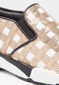 Baskets slip-on avec bordure noire, semelle blanche et un motif damier doré et blanc en sequins sur le tissu supérieur.
