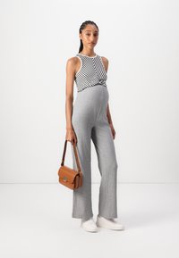 Grauer gestreifter Jumpsuit kombiniert mit einem ärmellosen Oberteil in schwarz-weißen Streifen. Die Accessoires bestehen aus einer braunen Handtasche mit Klappenverschluss und weißen Sneakers.