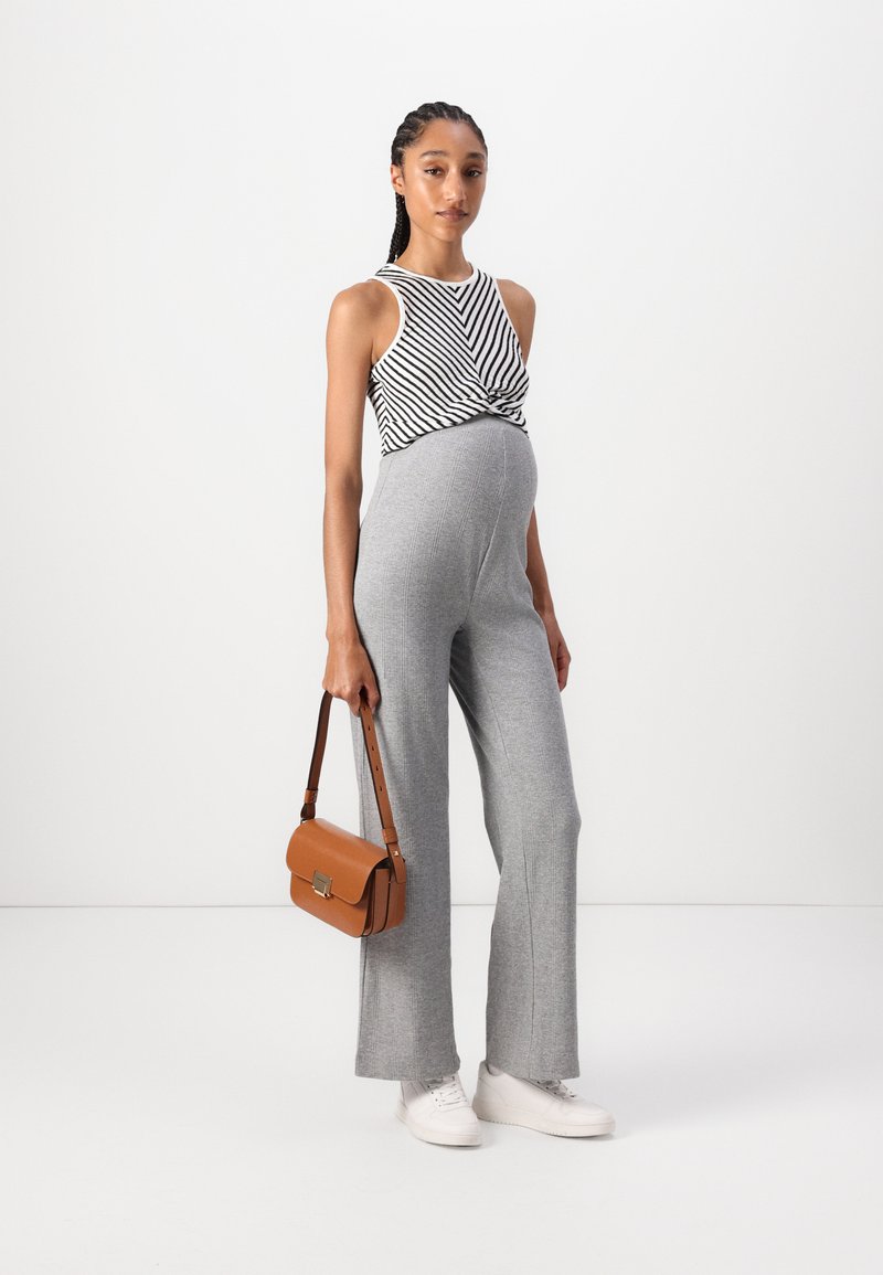 Grauer gestreifter Jumpsuit kombiniert mit einem ärmellosen Oberteil in schwarz-weißen Streifen. Die Accessoires bestehen aus einer braunen Handtasche mit Klappenverschluss und weißen Sneakers.